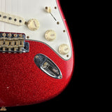 Close-up of a red glitter electric guitar body with cream control knobs, a white pickguard, and a chrome pickup cover against a black background.