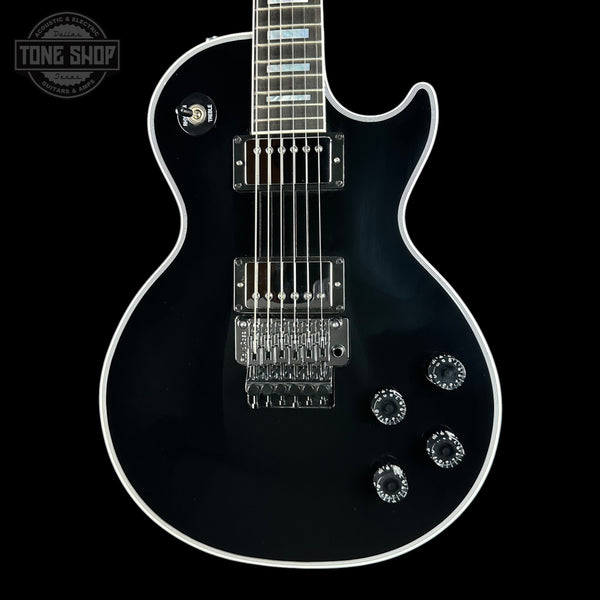 A black electric guitar with a glossy finish, chrome hardware, and white binding, shown against a solid black background with a Tone Shop watermark in the top-left corner.