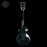 A black electric guitar shown from the back against a solid black background, with a Tone Shop logo watermark in the top-left corner.