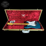 A teal blue electric guitar with a white pickguard and yellow maple neck, displayed inside an open gold hard case with red velvet lining. The Tone Shop logo is visible in the top left corner.