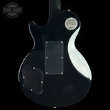 The back of a black Gibson electric guitar, showing the glossy finish, a silver circular Gibson logo badge, and a clear pickguard on a solid black background.