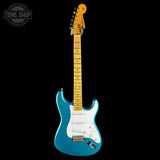 A blue electric guitar with a maple neck and white pickguard, photographed against a solid black background. A Tone Shop watermark is visible in the top-left corner.