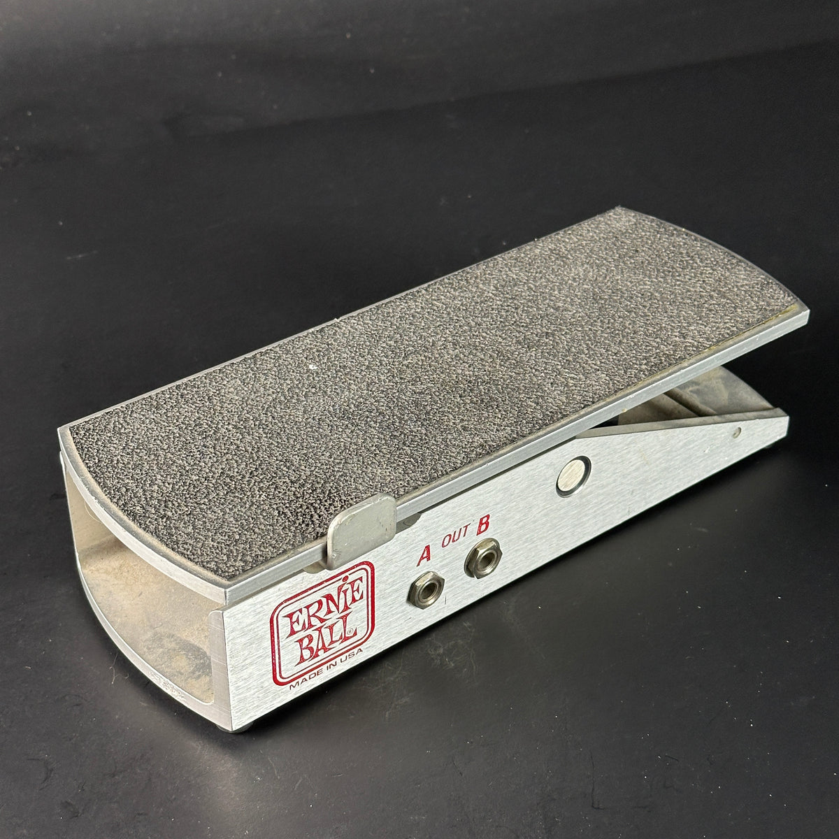 Metal foot pedal with textured surface and 'Ernie Ball' branding on a black background