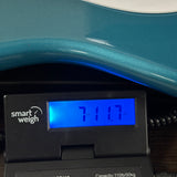 A close-up of a digital smart weigh scale displaying 711.7 oz on its blue backlit screen, positioned under a teal metallic surface.