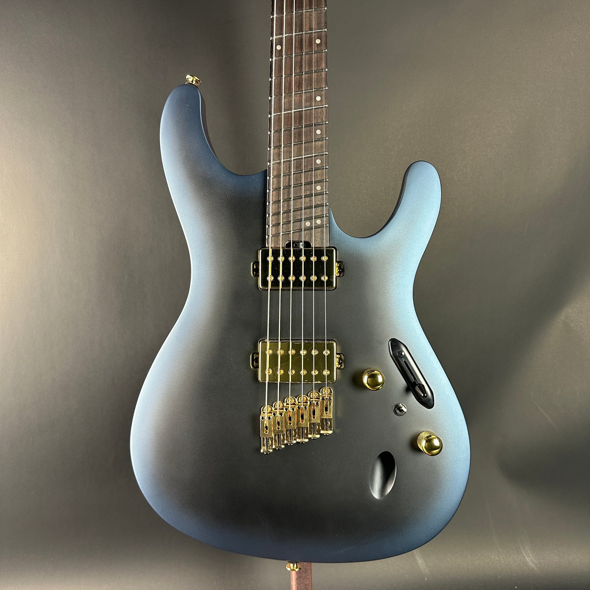 Gray electric guitar with gold hardware on a gray background