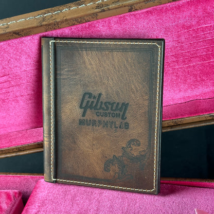 Brown leather notebook with 'Gibson Custom Murphy Lab' branding on a pink background