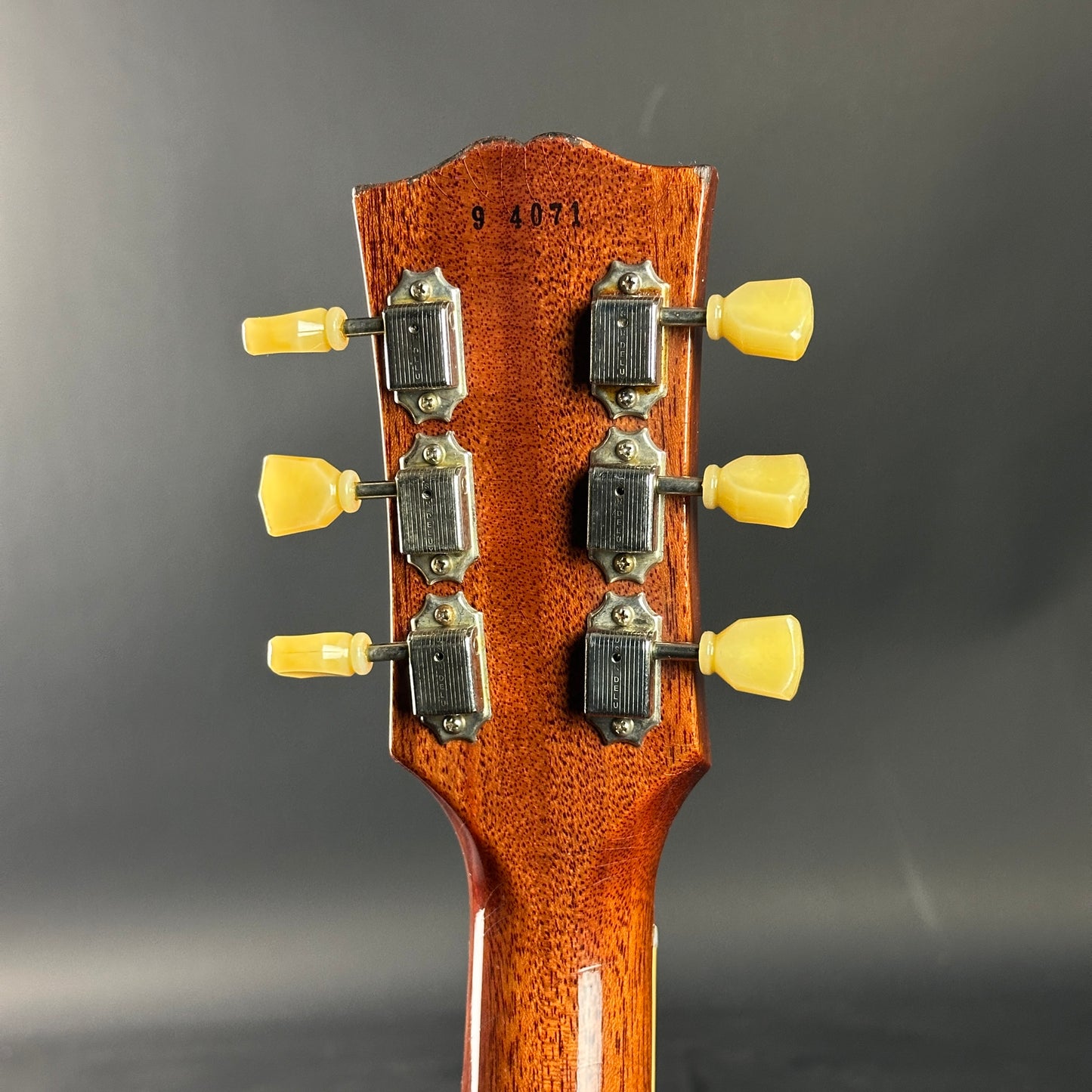 Close-up of a guitar headstock with tuning pegs on a gray background
