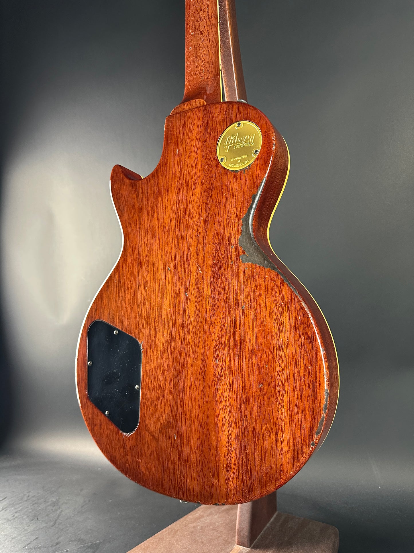 Close-up of a wooden guitar body with a visible brand logo on a gray background