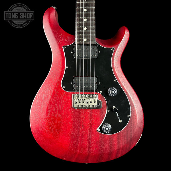 Red electric guitar with a black pickguard on a black background, featuring 'Tone Shop' branding.
