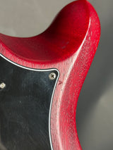 Close-up of a red guitar neck with a black pickguard on a blurred background