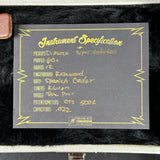 A close-up of a black instrument specification card with yellow handwritten text and border, placed on a black felt surface. The card includes details such as pickups, profile, radius, fingerboard, body, tuners, bridge, potentiometers, and capacitors, plus a small Fender logo at the bottom.