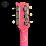 Close-up of the headstock of a pink electric guitar with yellow paint splatters, featuring silver tuning machines and cream tuning pegs, set against a solid black background.