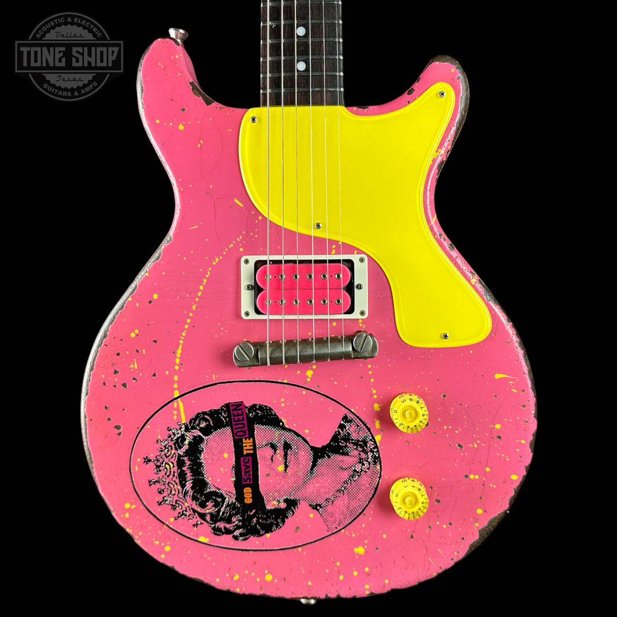 A pink electric guitar with a bright yellow pickguard, yellow knobs, and a distressed finish, featuring a black and white graphic of a woman on the lower left side. The neck is black with white dot inlays.