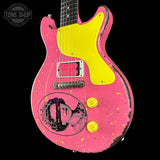 A custom electric guitar with a distressed pink finish, a bright yellow pickguard, and yellow control knobs, featuring a graphic of a woman's face on the lower bout.