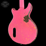 A close-up of a pink electric guitar body with distressed paint splatters and a dark wood patch, shown against a black background with a Tone Shop watermark in the top left.