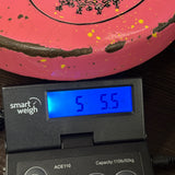 A pink disc golf disc with yellow and black speckles sits on top of a digital smart weigh scale displaying 5.5 lbs.