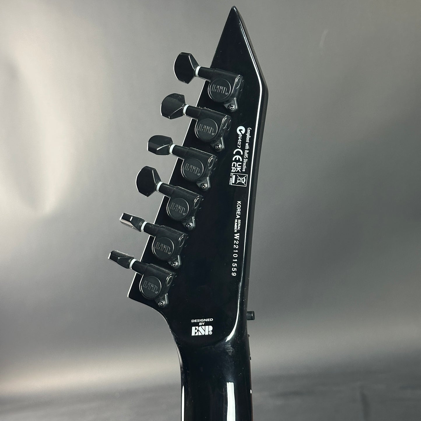 Close-up of a black electric guitar headstock with brand logos on a gray background