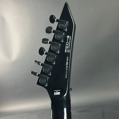 Close-up of a black electric guitar headstock with brand logos on a gray background