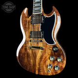 A double-cutaway electric guitar with a glossy natural flamed maple wood body, black pickguard, and gold hardware, shown against a solid black background with a Tone Shop watermark in the top left corner.