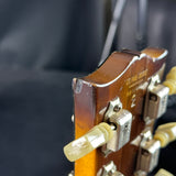 Close-up of a guitar's headstock with tuning pegs and brand name.