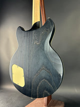 Close-up of a guitar body with a dark wood finish and gold hardware on a gray background