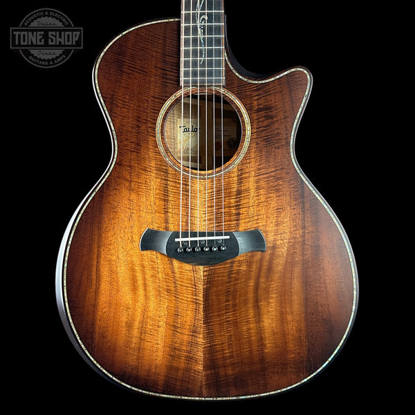Acoustic guitar with a dark brown finish on a black background, featuring the Tone Shop logo.