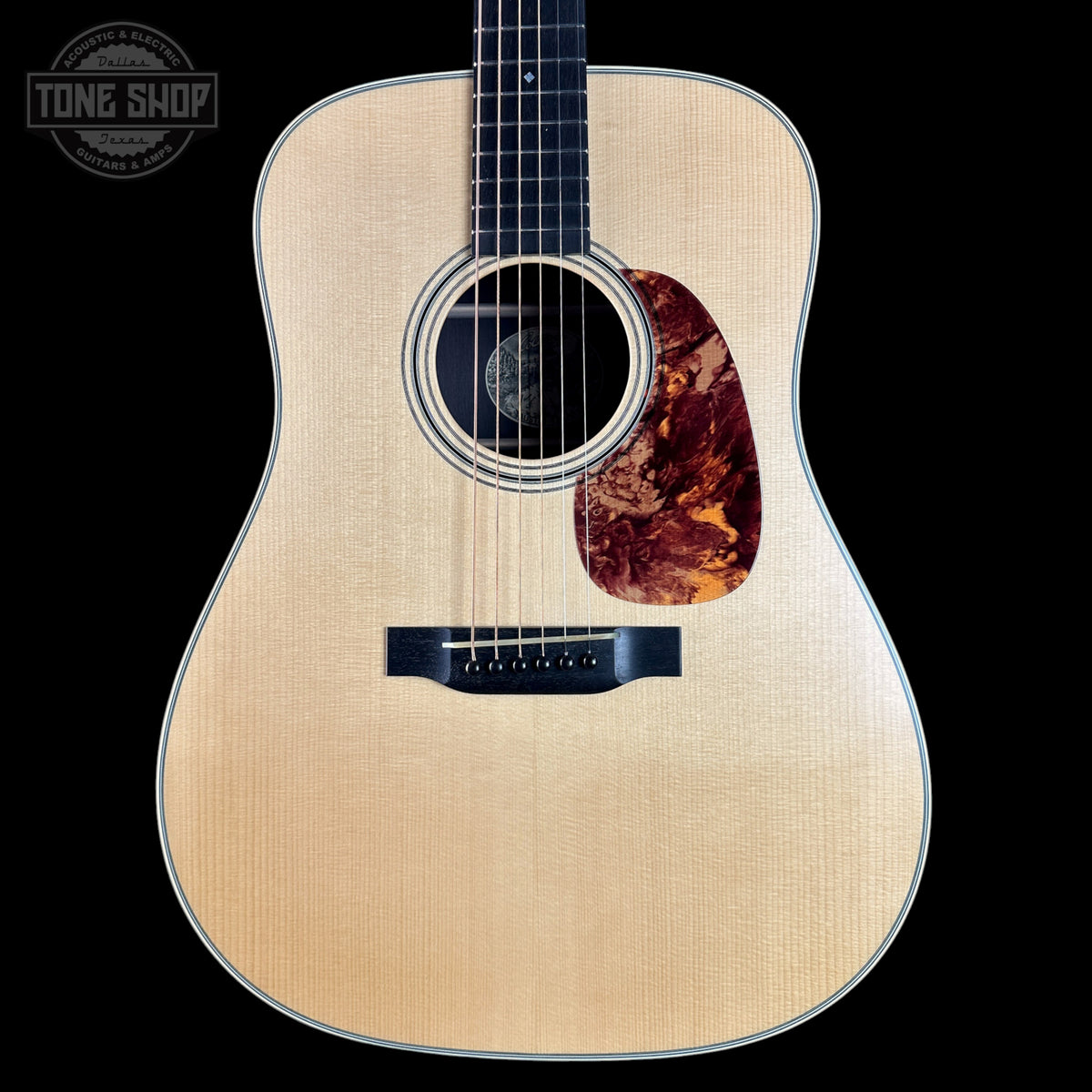 Acoustic guitar with a tortoiseshell pickguard on a black background, featuring the Tone Shop logo.