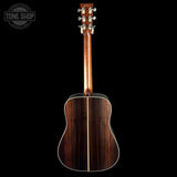 Acoustic guitar with a dark wood finish on a black background, featuring the Tone Shop logo.
