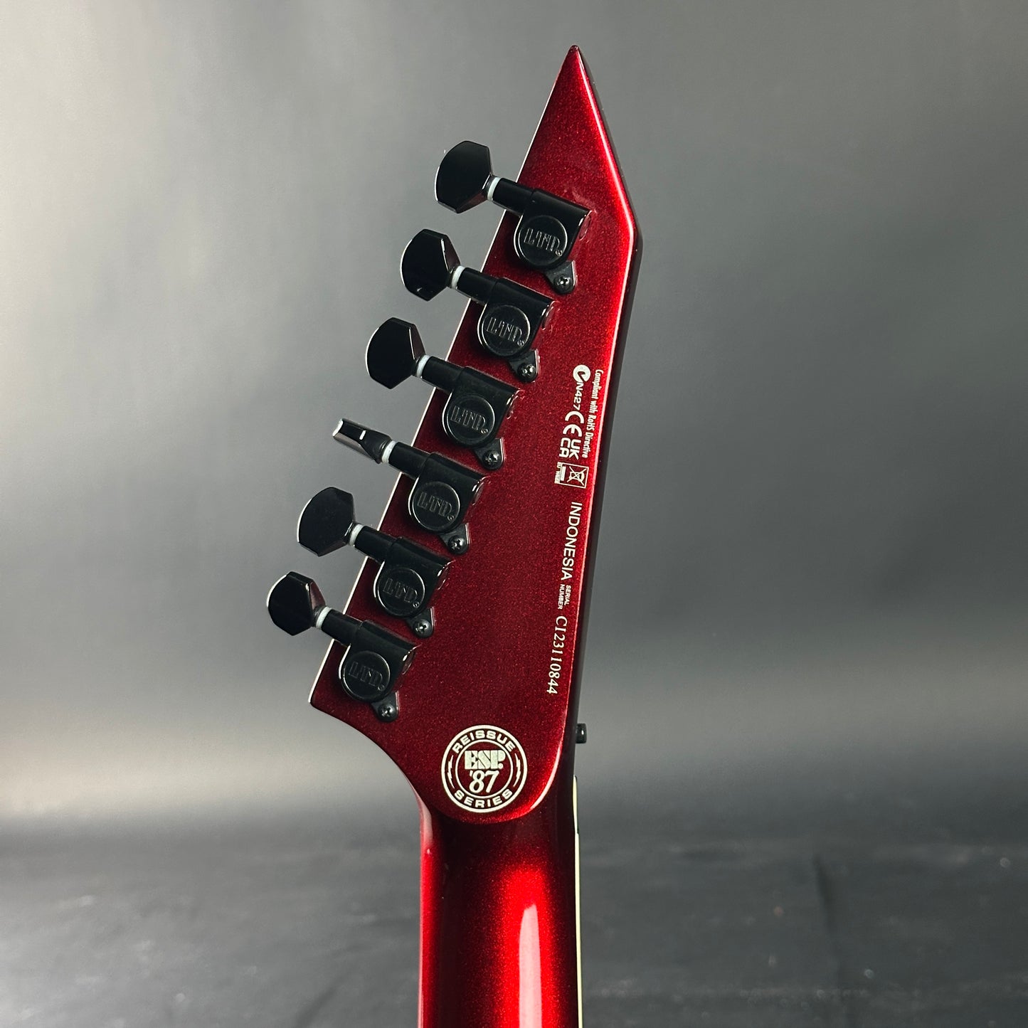 Close-up of a red guitar headstock with tuning pegs on a gray background