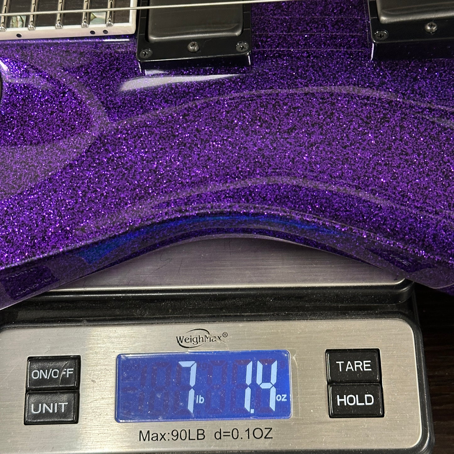 Purple glittery guitar on a digital scale displaying weight.