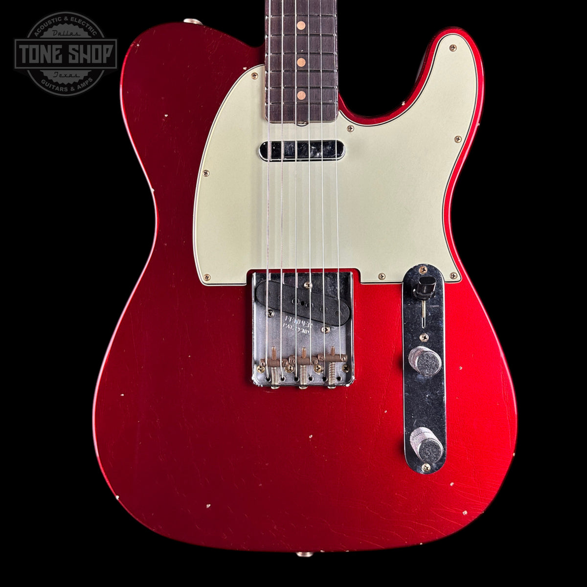 Red electric guitar with a white pickguard on a black background, featuring the Tone Shop logo.