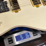 Digital scale displaying weight of a guitar, with a close-up of the guitar's neck and headstock.