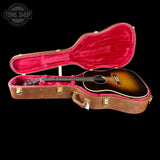 Acoustic guitar in a brown case with red interior on a black background, featuring 'Tone Shop' logo.