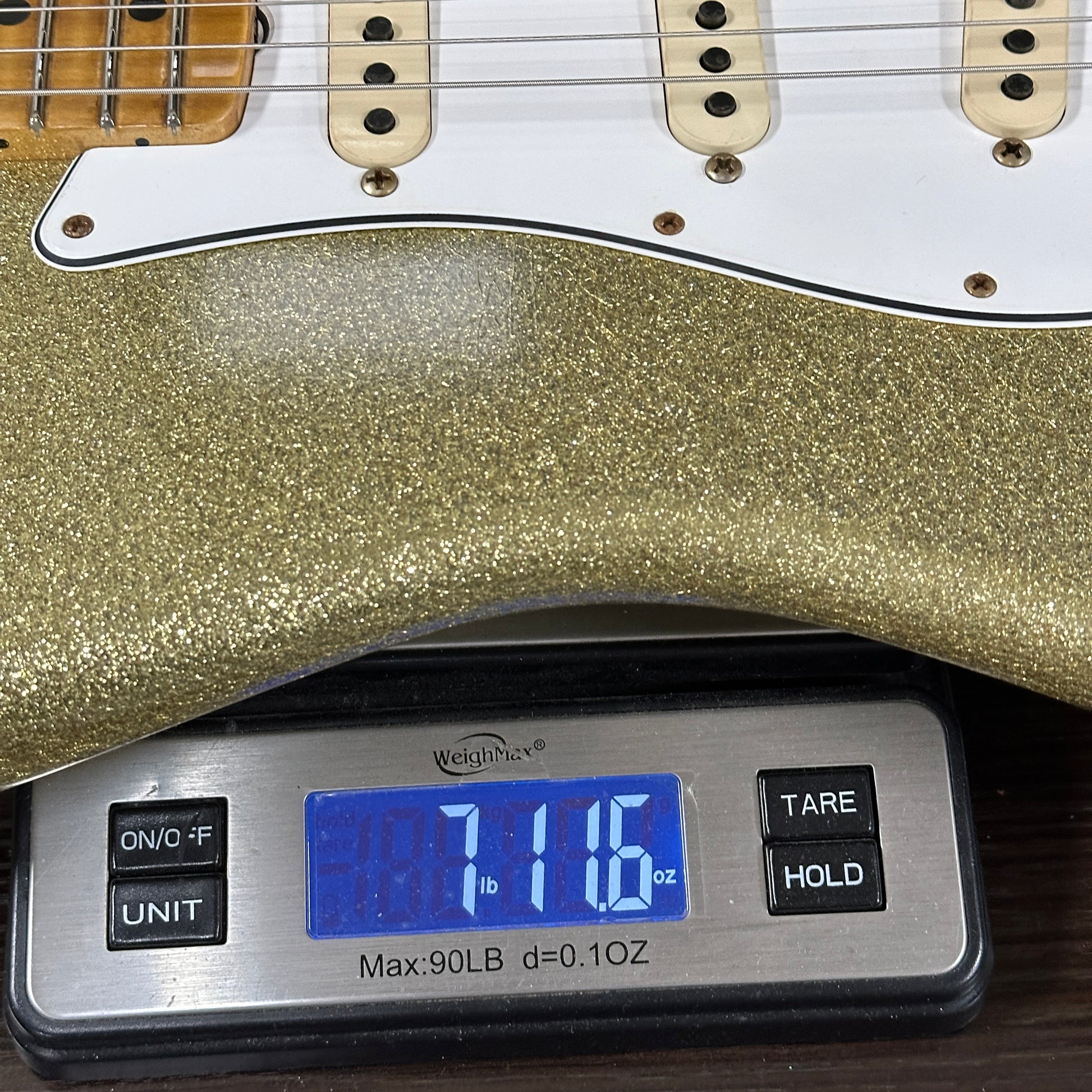 Gold glittery electric guitar on a digital scale displaying weight.