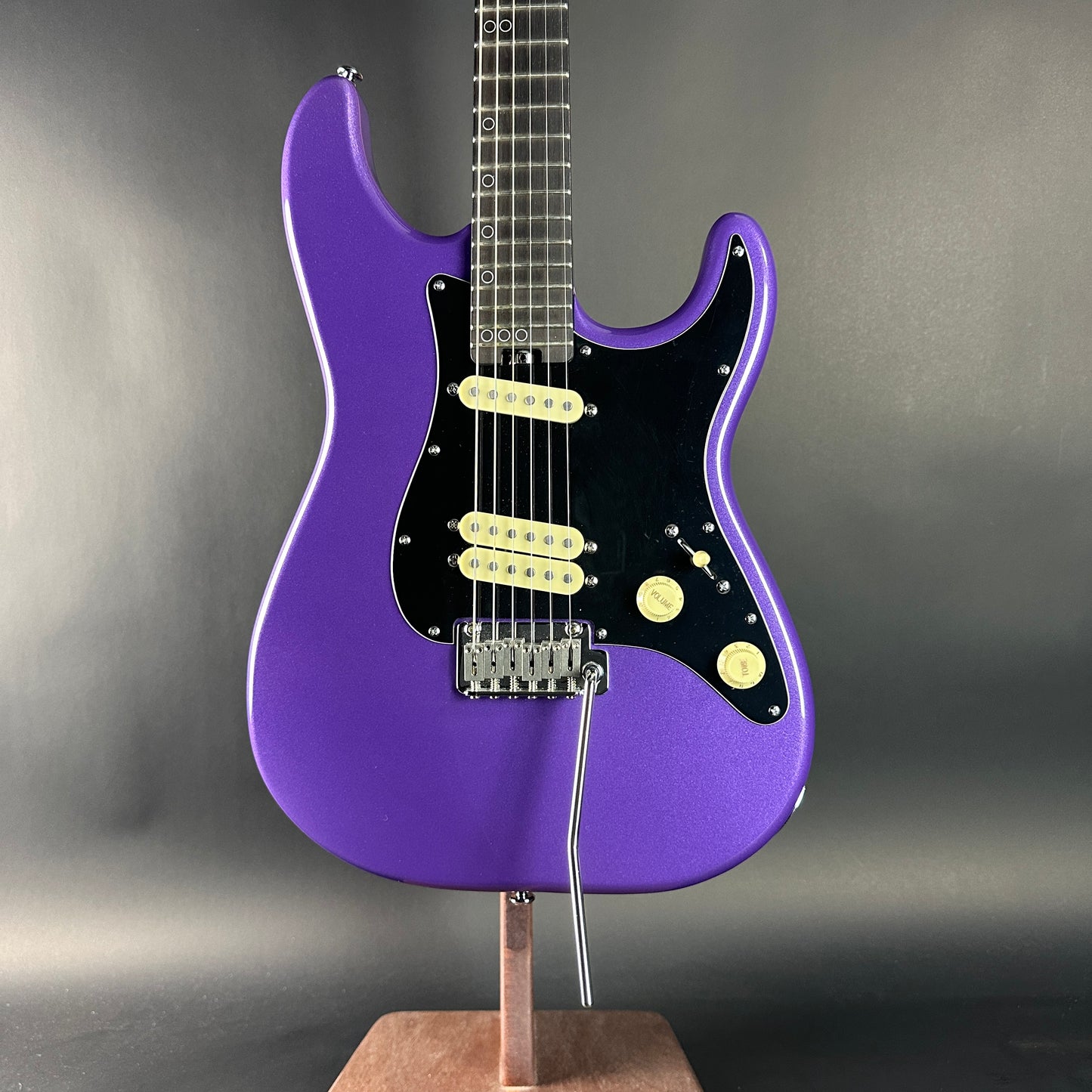 Purple electric guitar on a stand against a gray background