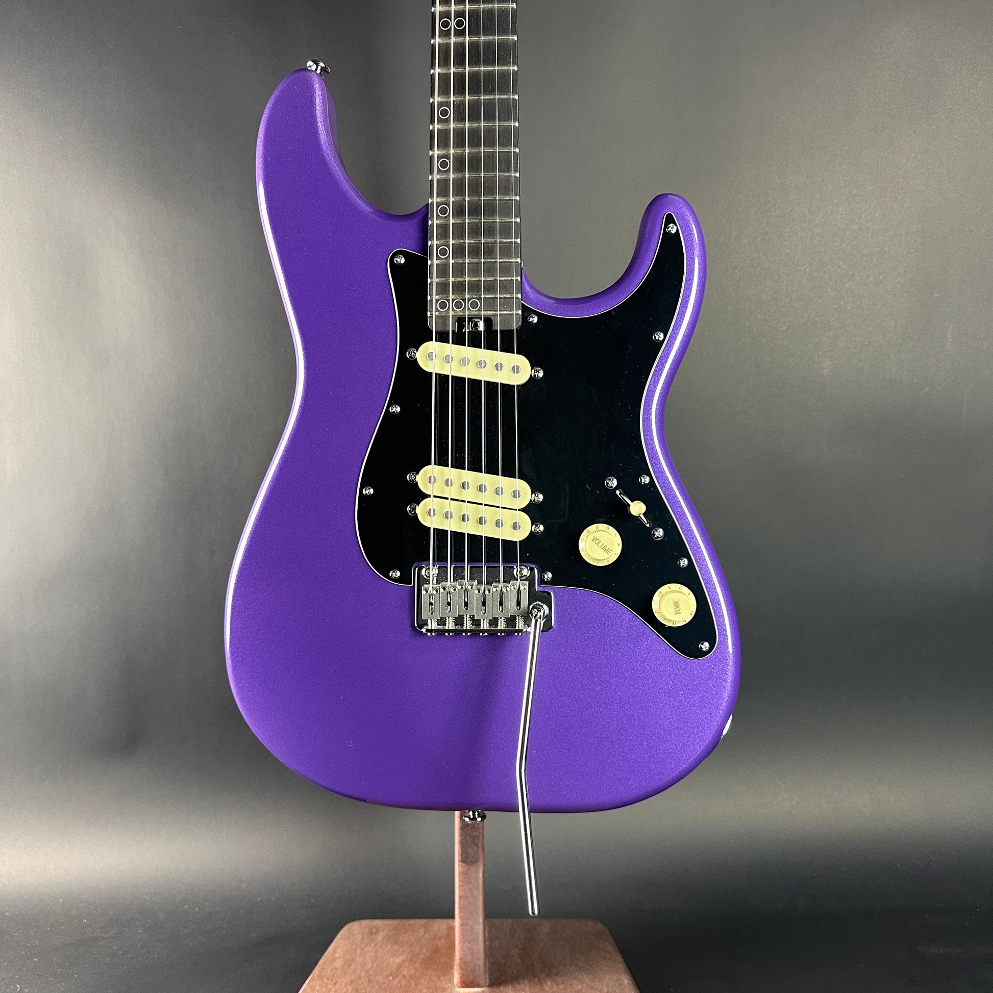 Purple electric guitar on a stand against a gray background