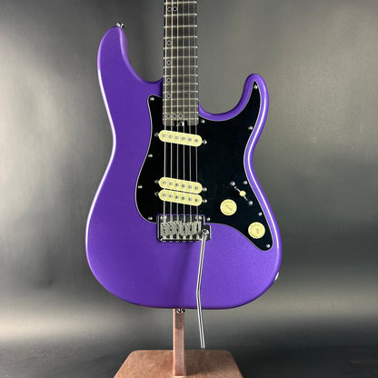 Purple electric guitar on a stand against a gray background