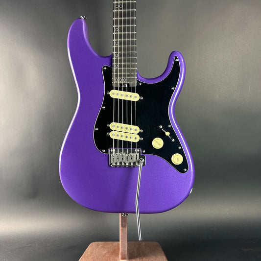 Purple electric guitar on a stand against a gray background