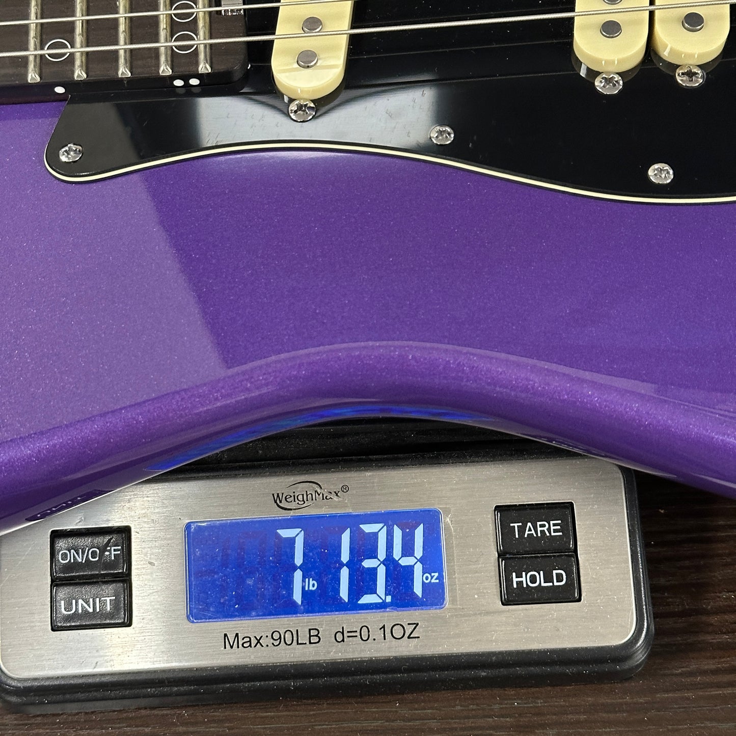 Purple electric guitar on a digital scale displaying weight.