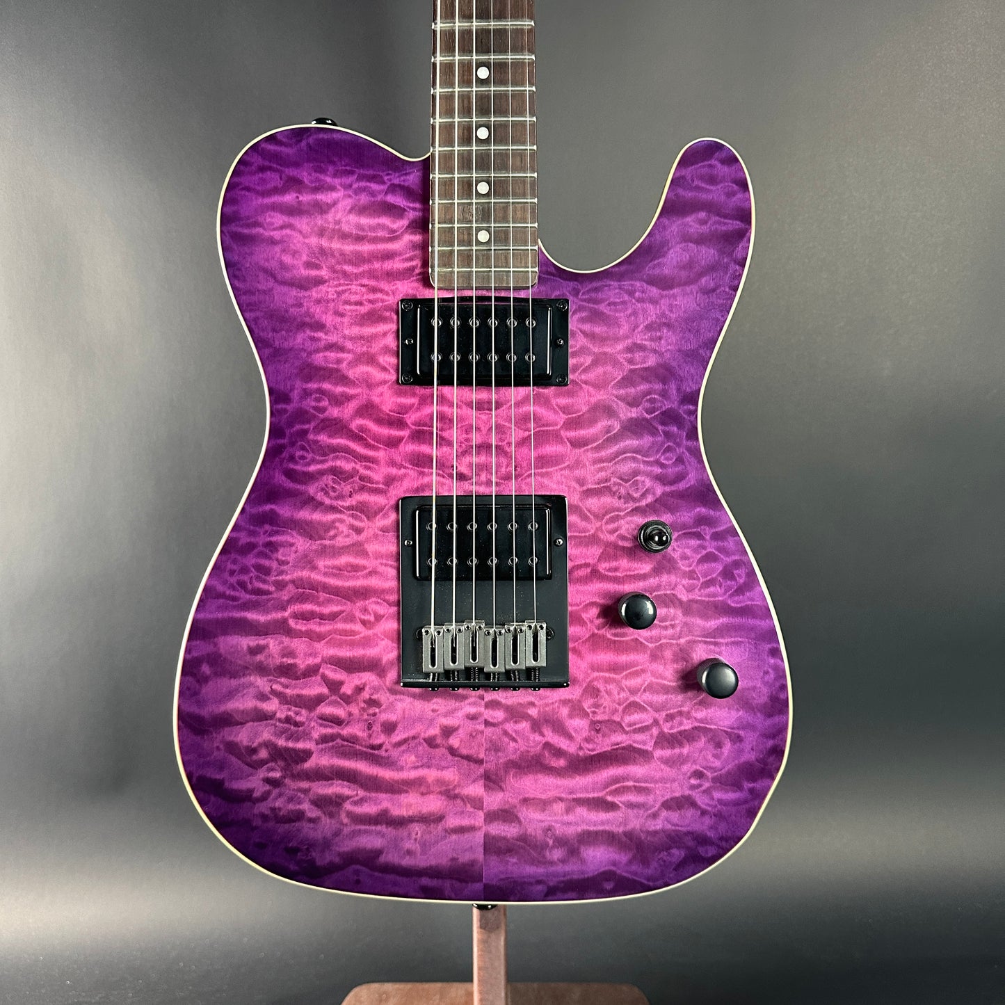 Purple electric guitar on a stand against a gray background