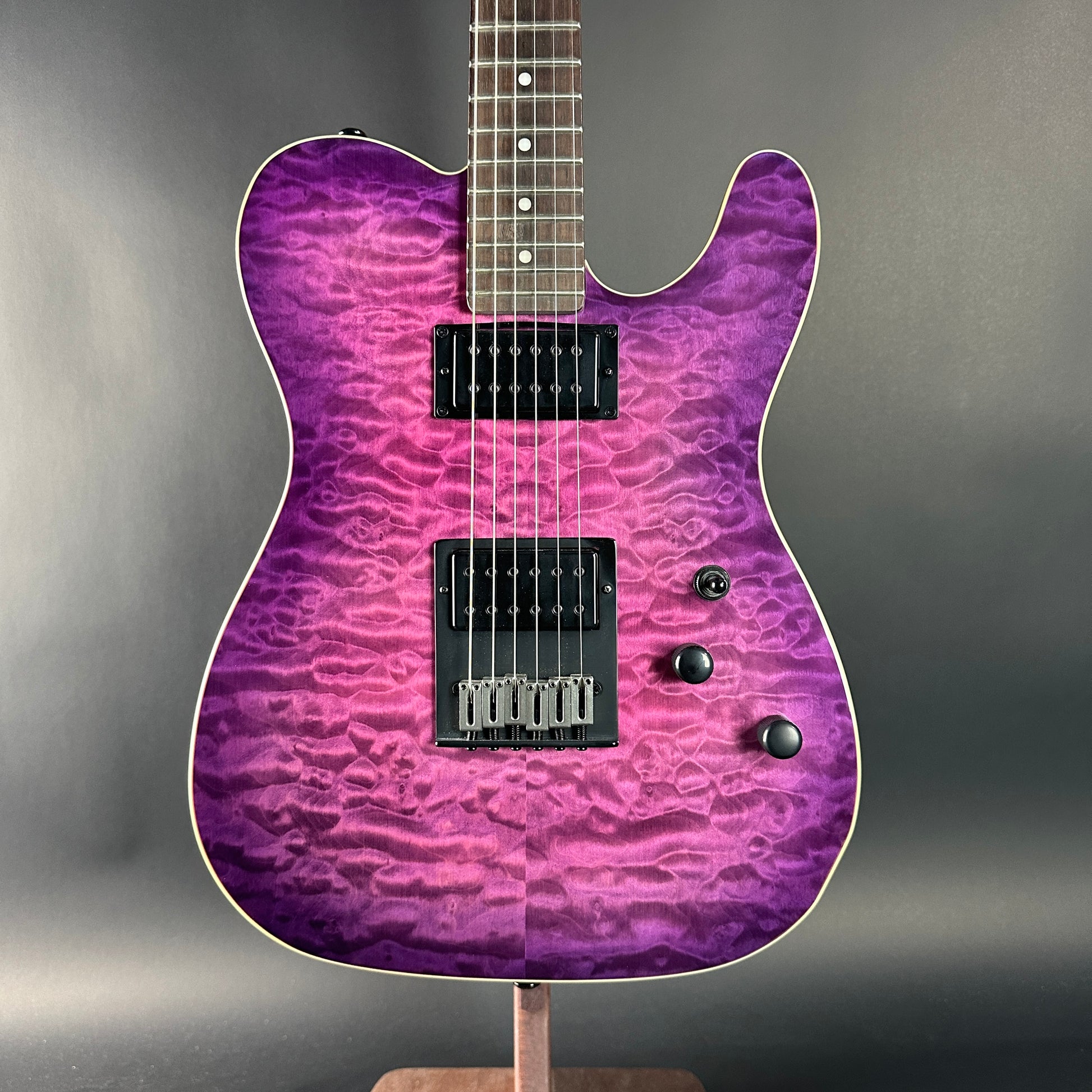 Purple electric guitar on a stand against a gray background