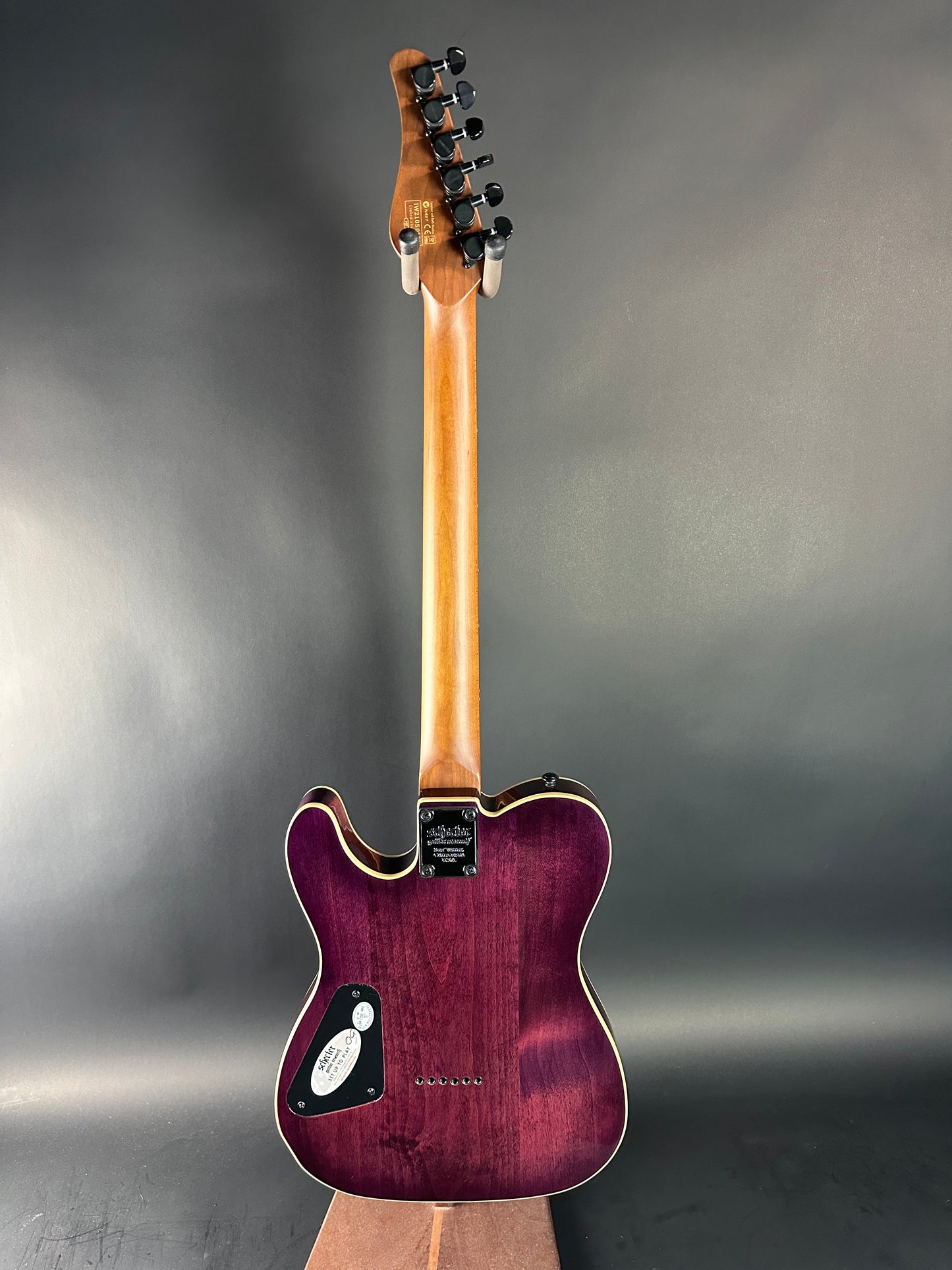 Electric guitar with a purple body and wooden neck on a gray background