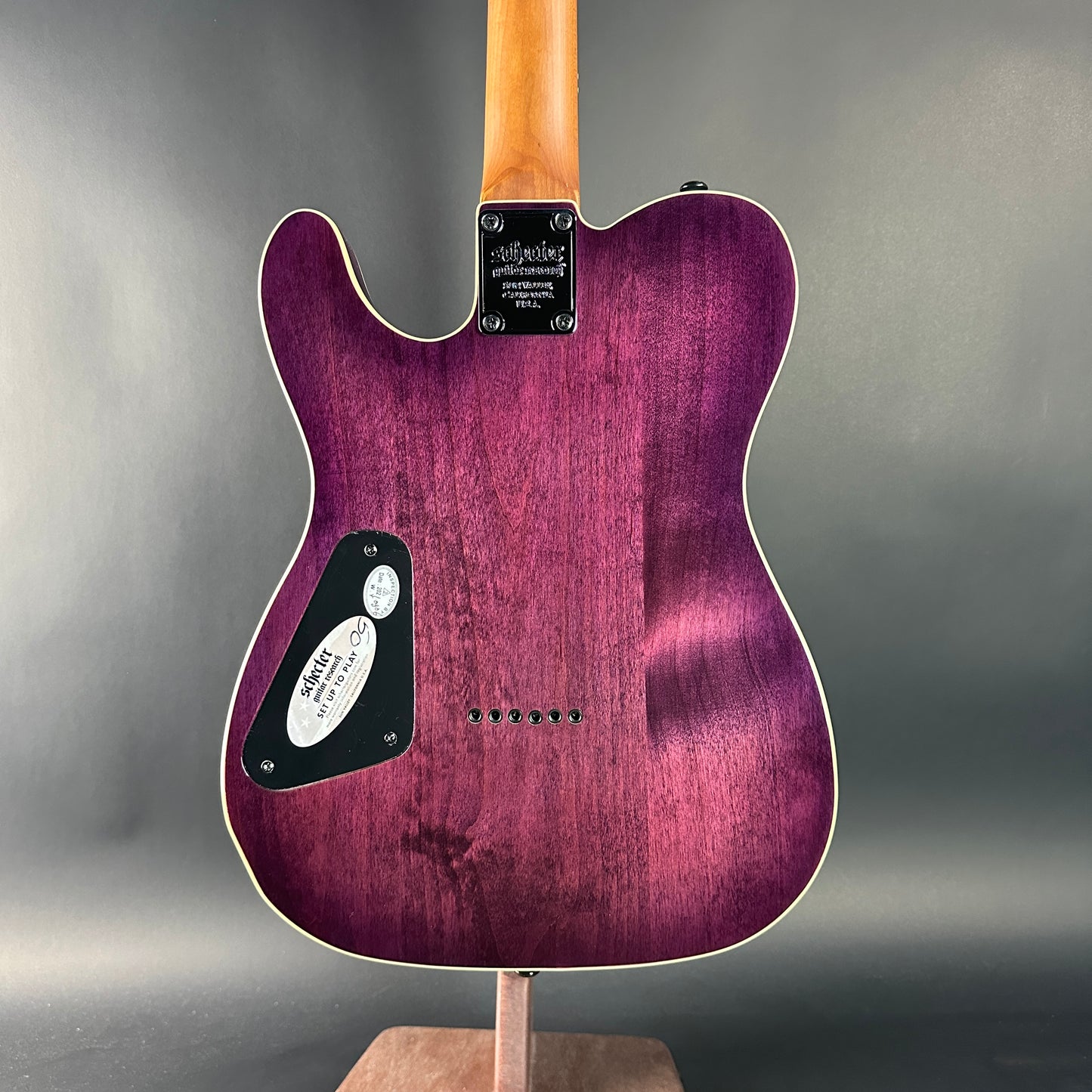 Purple electric guitar on a stand against a gray background