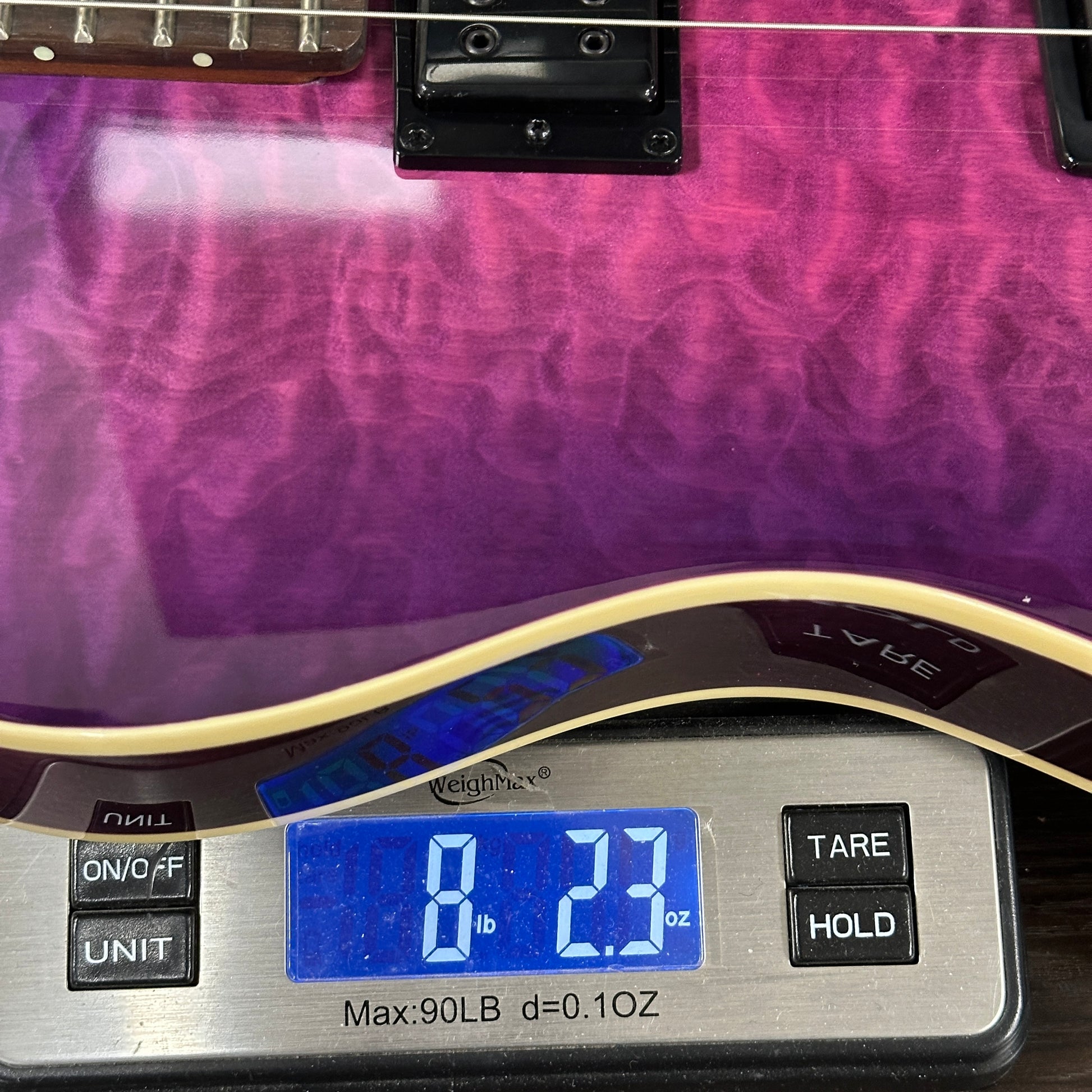 Purple electric guitar on a digital scale displaying weight
