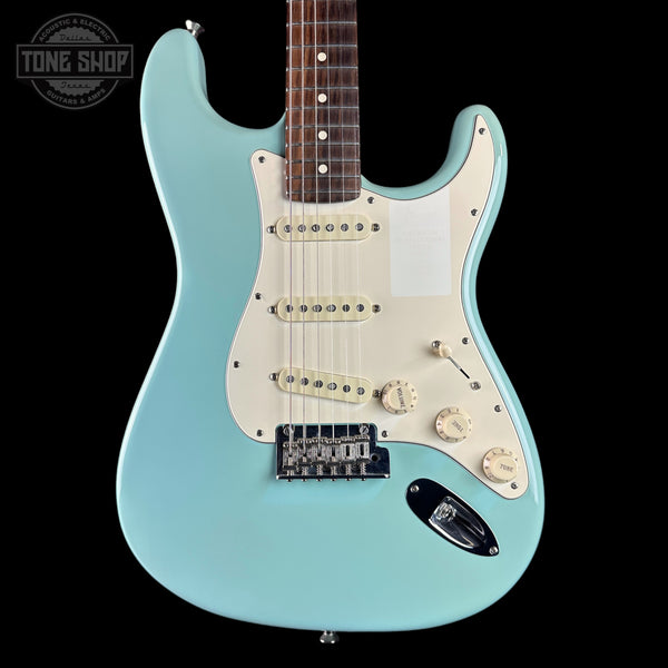 A light blue electric guitar with a cream pickguard and cream control knobs, shown against a solid black background. A Tone Shop logo is visible in the top-left corner.