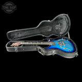 Blue electric guitar in a black case with 'Tone Shop' logo.