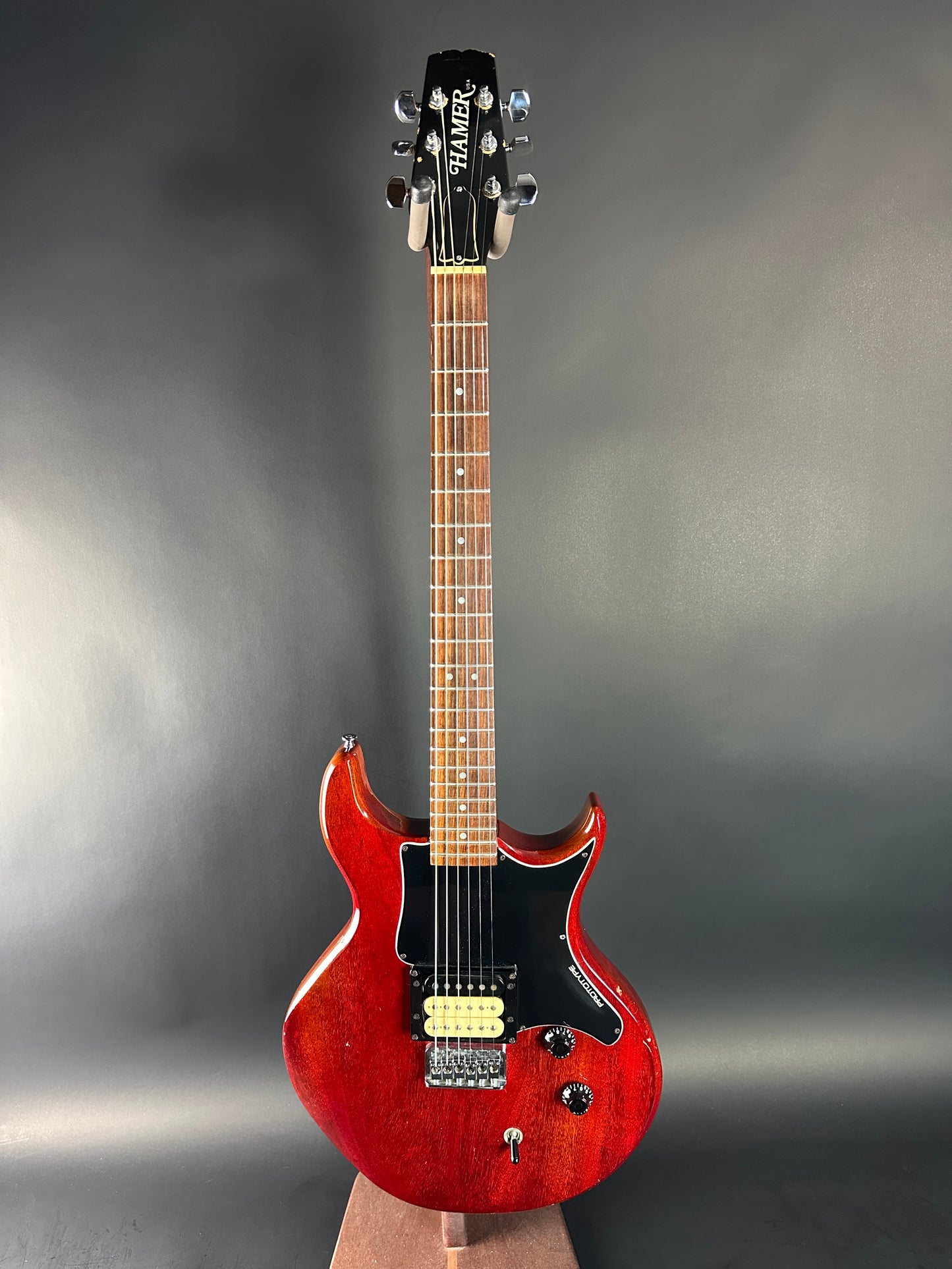 Electric guitar with a red body and black pickguard on a gray background