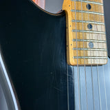 Close-up of a black electric guitar body and maple fretboard with metal strings and circular fretboard inlays.