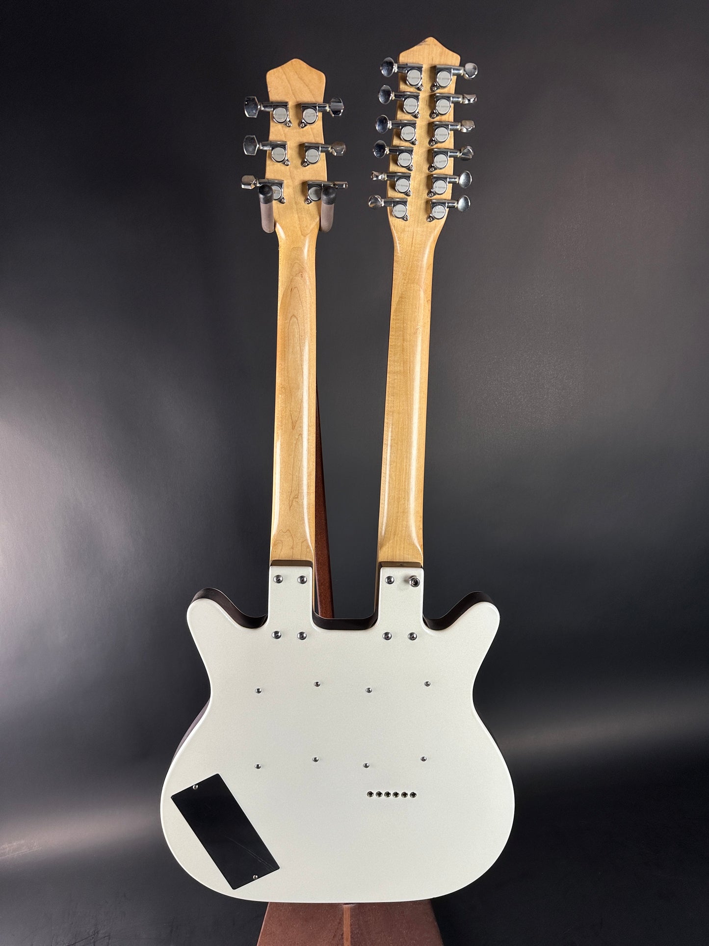 Double-neck electric guitar with white pickguard on a dark background
