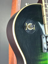 Close-up of an electric guitar body showing a black glossy finish with a green flame gradient at the upper right, a gold-toned edge trim, and a black round switch labeled RHYTHM and TREBLE.
